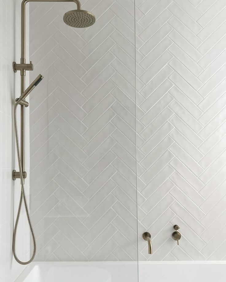 the shower head is mounted on the wall next to the bathtub, which has a herringbone pattern