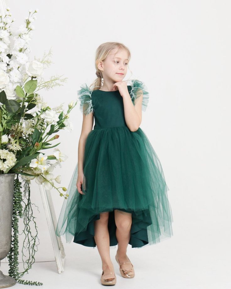 "Embark on a journey to your \"Emerald Dream\" with this enchanting green tulle dress. Every detail of this dress is designed to captivate, from the satin base delicately veiled with tulle to the meticulous craftsmanship, this dress ensures comfort. The hemline, gracefully shorter in the front and gently cascading longer in the back, adds a touch of whimsy to the ensemble, allowing you to glide through any event with grace and charm. But what truly sets the \"Emerald Dream\" apart are the small Green Princess Dress For Fancy Events, Green Princess Style Fancy Dress, Green Princess Dress For Fancy Dress Event, Green Princess Style Dress For Fancy Dress Event, Green Princess Dress For Fancy Dress, Green Tulle Princess Dress For Fancy Dress, Green Tulle Dress For Dress-up, Dark Green Ruffled Dress For Party, Green Tulle Fairy Dress For Party