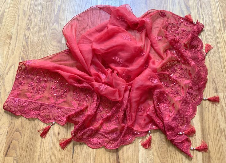 This is a red scarf or wrap with embroidered flowers and leaves motifs in deep red. It is made of chiffon.  The embroidery is further embellished with pearls etched onto fabric using rounded metal pins. Unlike pasted pearls, these don't drop or come out with regular usage. Both long edges are hemmed with silk threads to prevent loose threads from coming out from the edges. Short edges have broad, intricate embroidered, and scalloped borders that end in silk tassels with pearl hangings.  Size = 8 Red Shawl-shaped Dupatta With Pallu, Red Traditional Drape Shawl For Eid, Red Dupatta Shawl With Pallu, Red Georgette Dupatta For Celebration, Red Dupatta With Pallu Shawl Shape, Bollywood Style Red Shawl With Pallu, Elegant Red Shawl With Resham Embroidery, Red Shawl With Traditional Drape For Festive Occasions, Red Embroidered Fabric With Sheer Dupatta For Eid