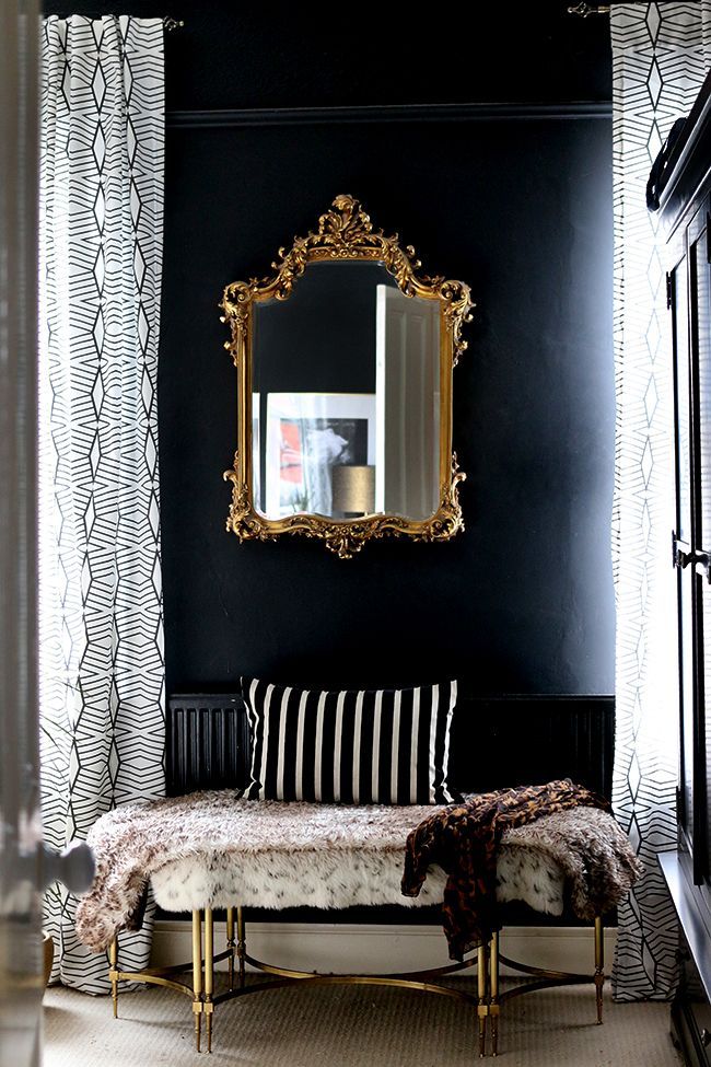 a black and white room with a gold framed mirror on the wall above a bench