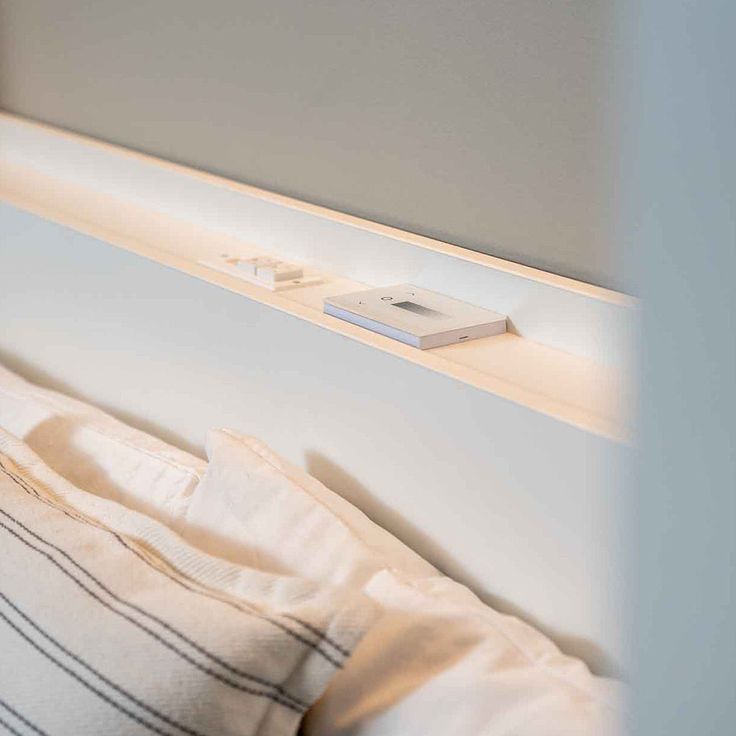 a close up of a bed with a book on the headboard and light above it