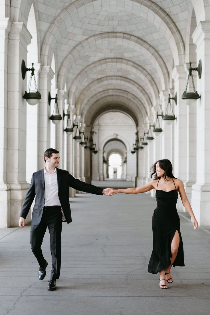 a man and woman holding hands while walking down an archway way with lanterns hanging from the ceiling