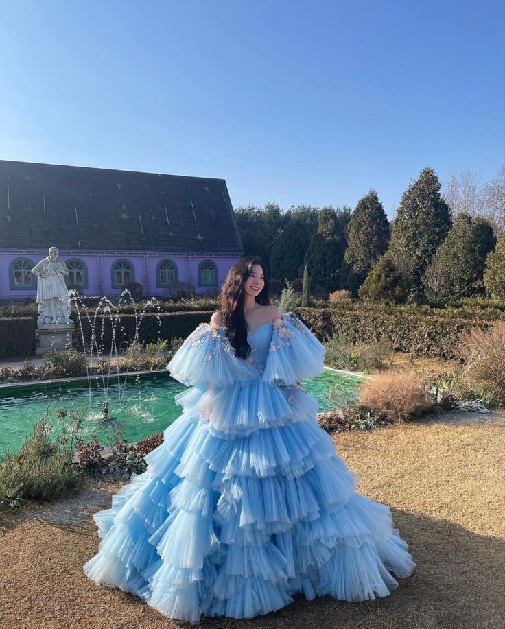 a woman standing in front of a fountain wearing a blue dress with ruffles