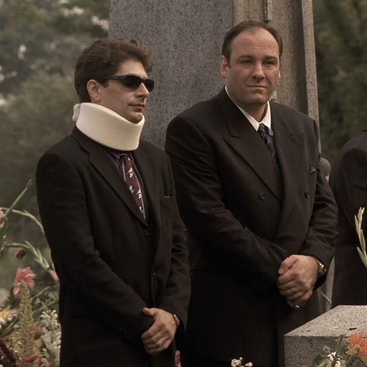 two men standing next to each other in front of a grave with flowers on it