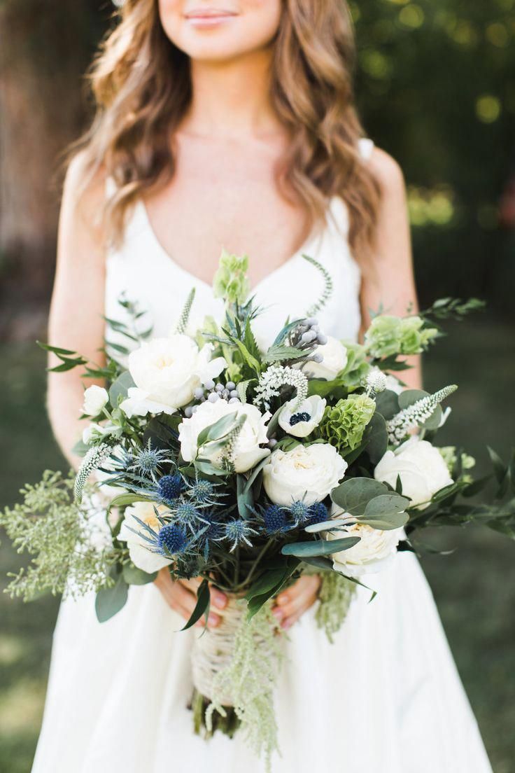 a woman holding a bouquet of white and green flowers in her hands with greenery