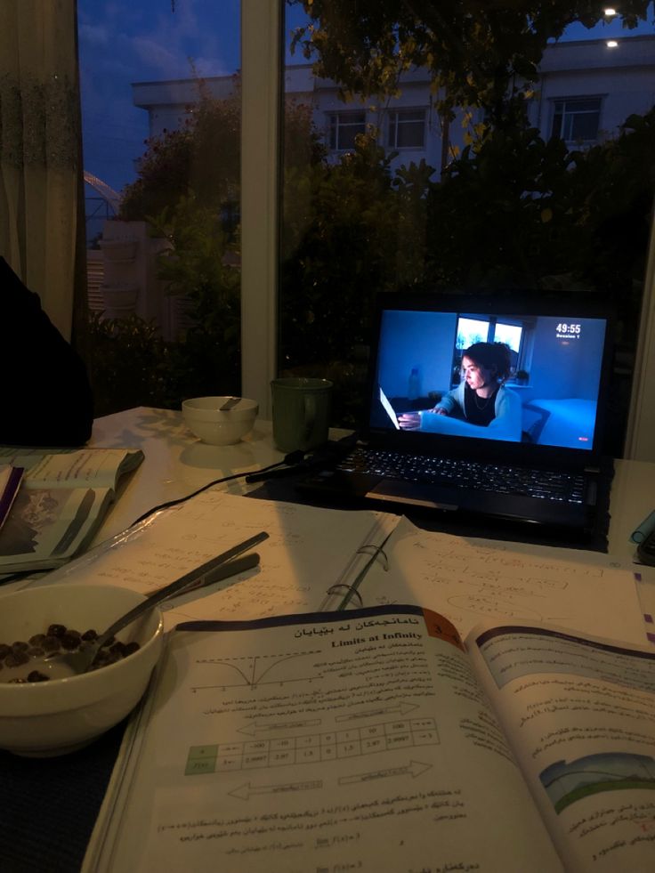 a laptop computer sitting on top of a table next to a bowl of food and a book