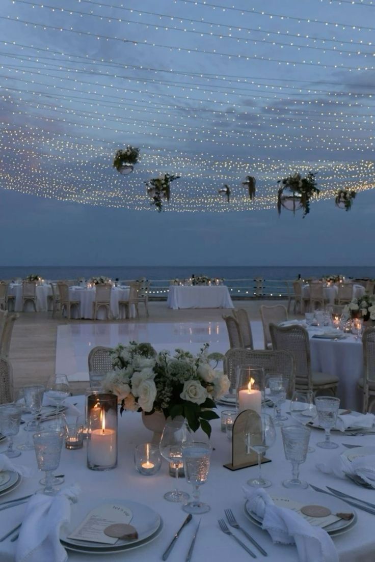 the tables are set with white linens and place settings for an elegant dinner on the beach