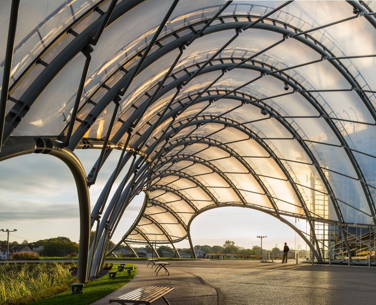 the sun shines through an arched glass building with benches under it and people walking in the distance