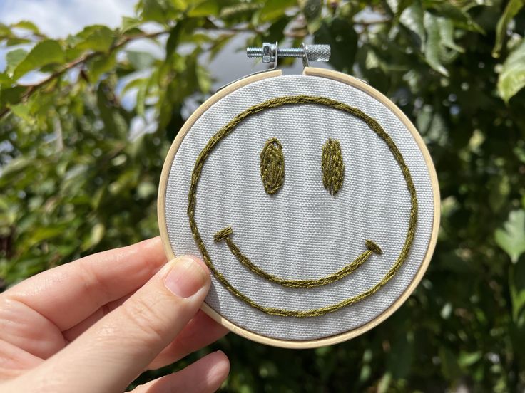 a hand embroidered smile face with two eyes on a white hoop hanging from a tree