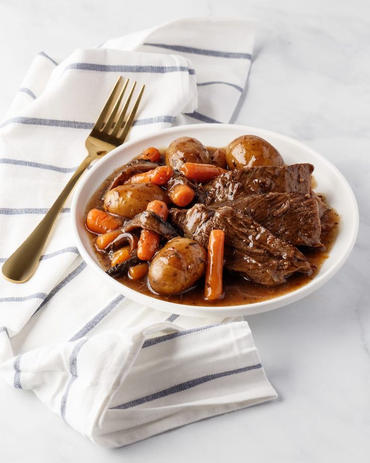 a white bowl filled with beef and carrots on top of a table next to a fork