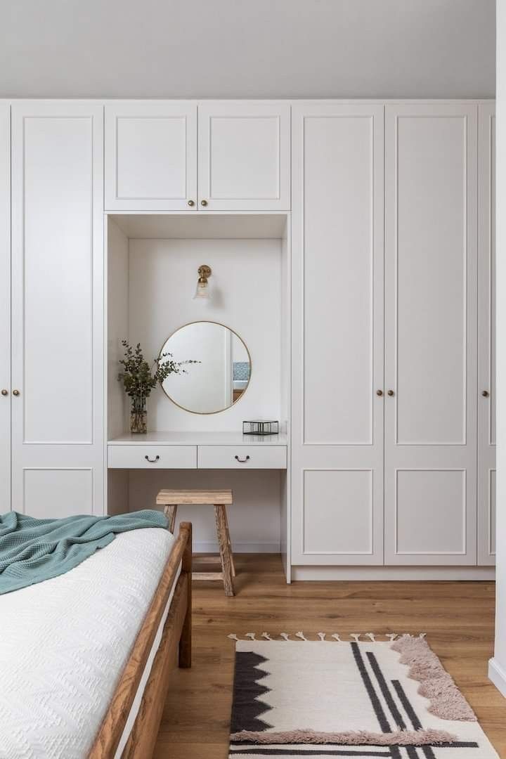 a bedroom with white cupboards and a large mirror on the wall above the bed