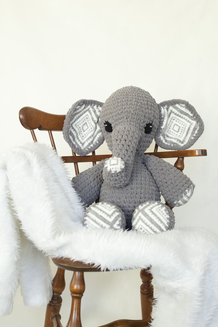 an elephant stuffed animal sitting on top of a wooden chair next to a white blanket