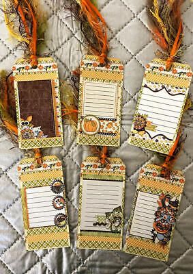 four tags with feathers attached to them sitting on a quilted bed spreadered in orange and brown