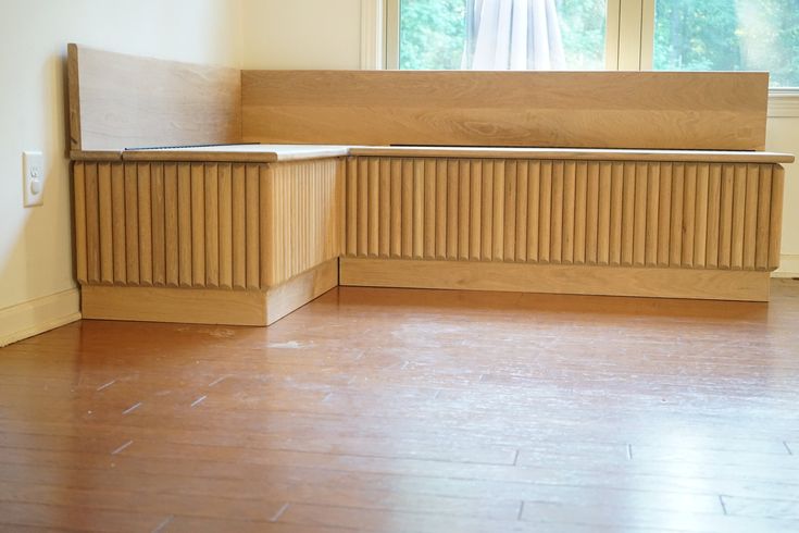 an empty room with a wooden bench in the center and windows behind it on both sides