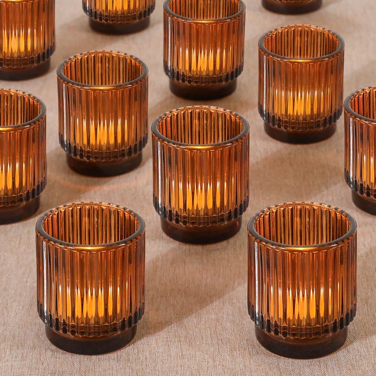 many brown glass cups sitting on top of a table next to each other with one candle in the middle