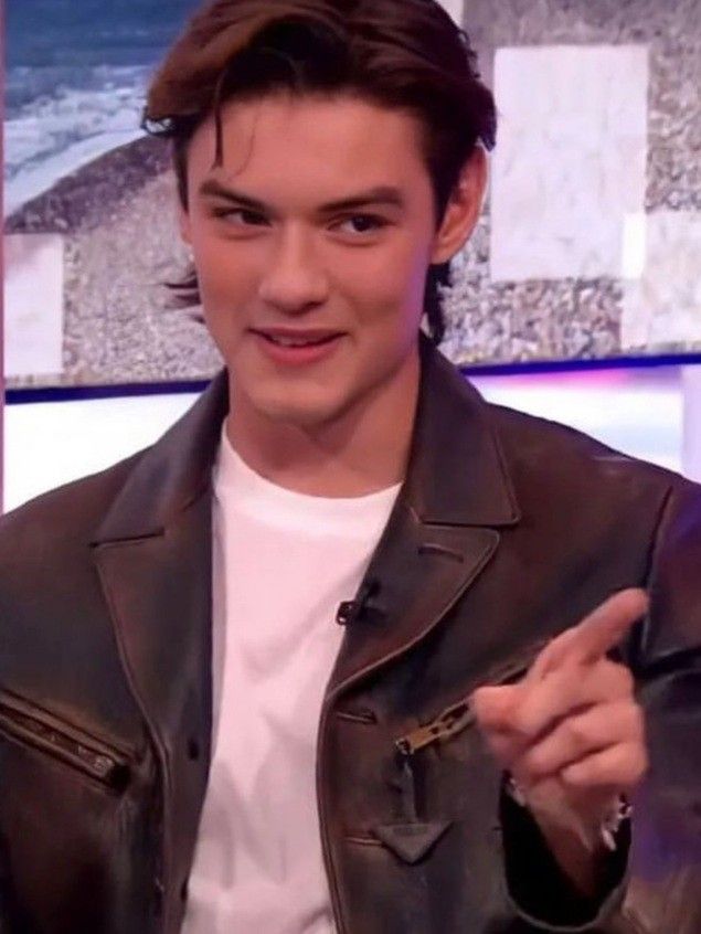 a young man wearing a leather jacket and white t - shirt is talking to someone