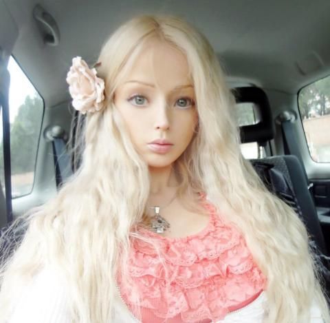 a woman with long blonde hair sitting in the back seat of a car wearing a pink top