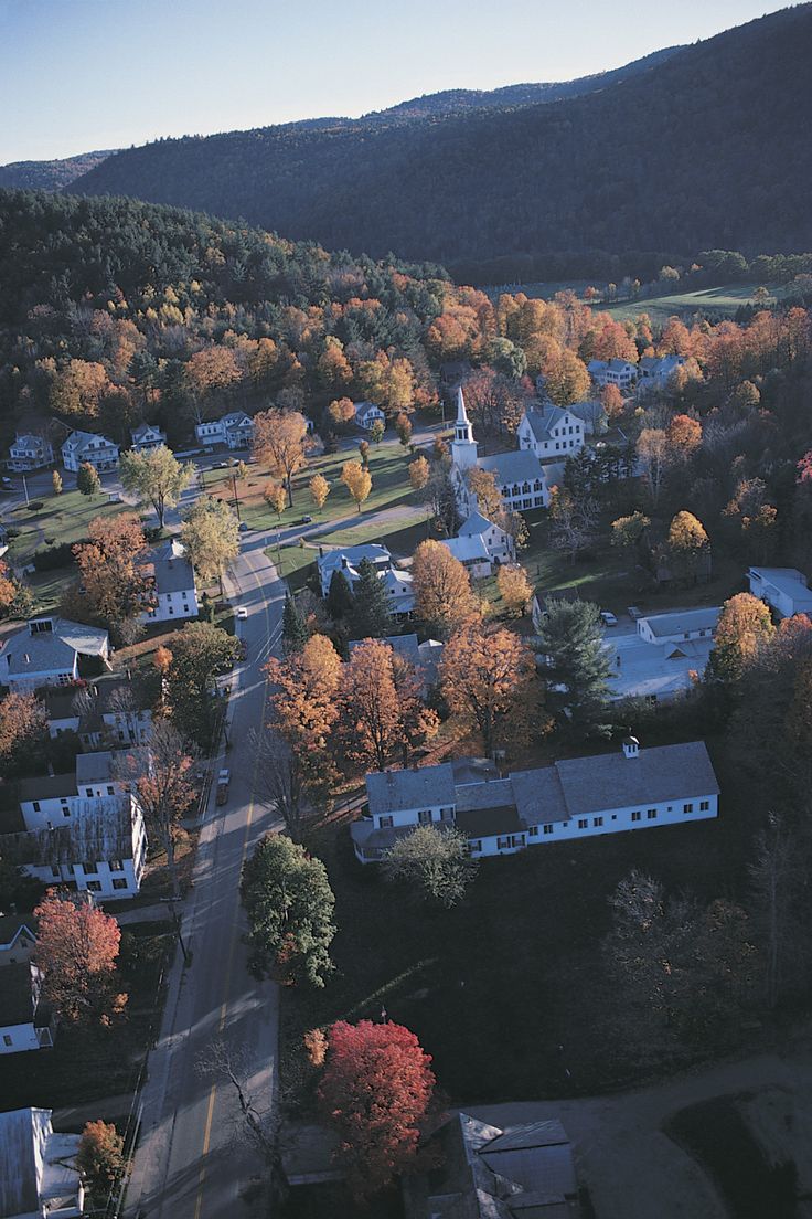 an aerial view of a small town surrounded by trees in the fall with colorful foliage