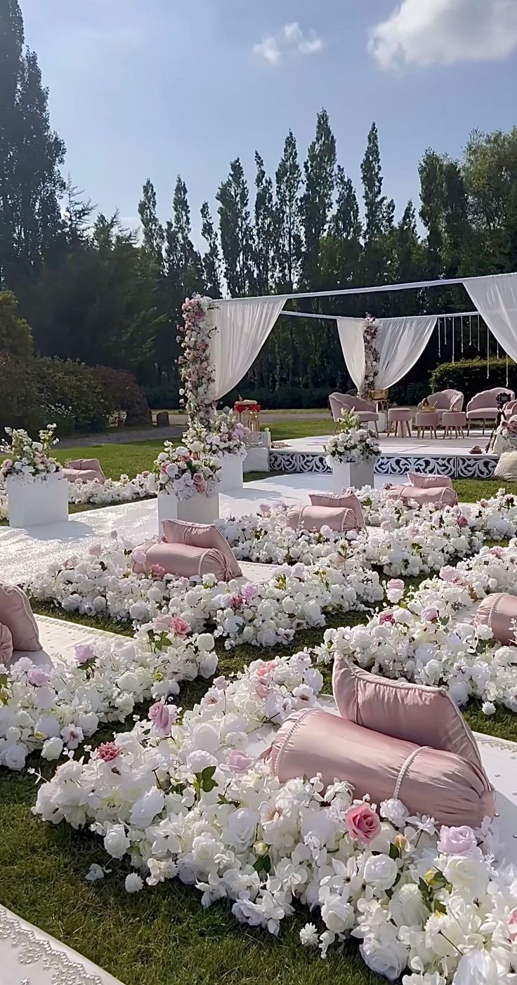 an outdoor wedding setup with pink and white flowers on the grass, couches and tables