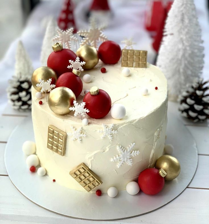 a white cake with red and gold decorations on it sitting on a table next to pine cones