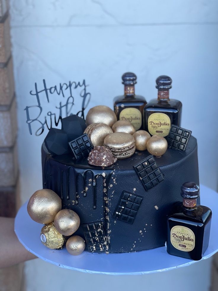 a birthday cake with gold decorations and bottles on the top is sitting on a table