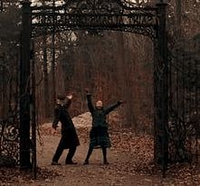 two people standing under an iron gate in the woods