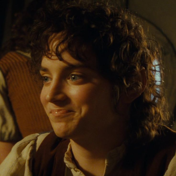 a young man with curly hair sitting on a couch looking at the camera and smiling