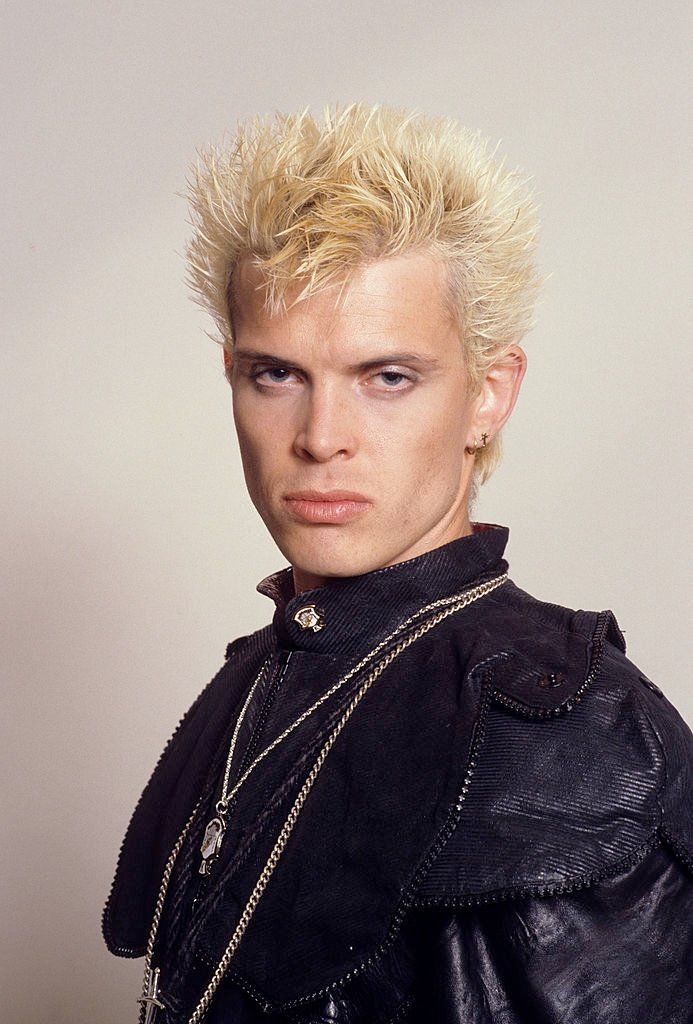 a man with blonde hair wearing a black leather jacket and chain around his neck is looking at the camera