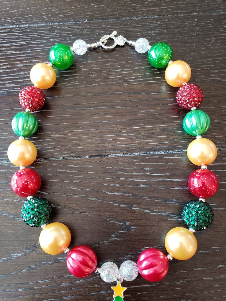 "Christmas Inspired Christmas Tree Children's Chunky Bubblegum Bead Necklace & Bracelet Set/ Holidays This very cute Christmas Tree Necklace & Bracelet Set is a perfect addition to any holiday outfit and the holiday season. The Necklace is made up primarily of 20mm beads in shades of red, green and yellow gold. The necklace measures approximately 11\" when toggled around neck including the Christmas Tree pendant. The Bracelet is an elastic bracelet, doubled up for extra strength. The Nec Holiday Festive Jewelry With Colorful Beads, Festive Holiday Jewelry With Colorful Beads, Multicolor Round Beads Christmas Jewelry, Christmas Party Beaded Necklaces With Round Beads, Christmas Party Round Bead Necklaces, Festive Christmas Beads With Round Shape, Festive Christmas Beads, Christmas Festive Round Beads, Multicolor Round Beads Jewelry For Holidays