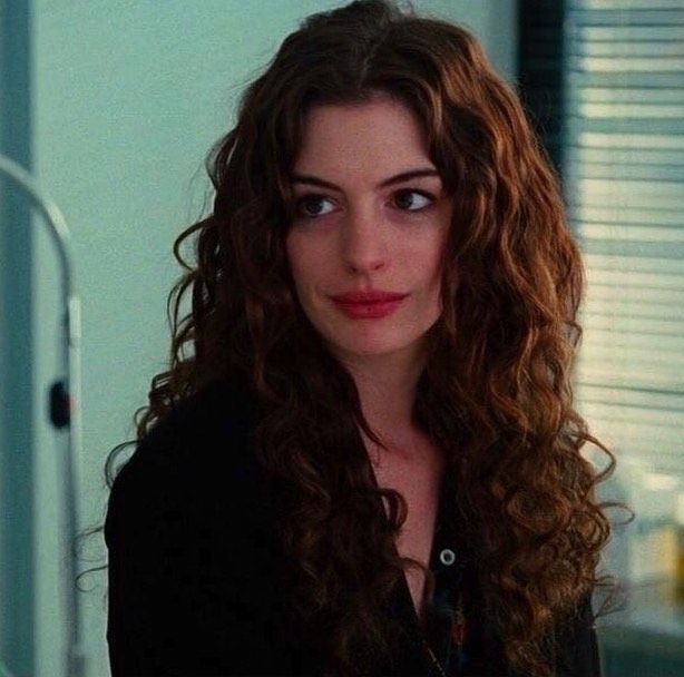 a woman with long curly hair standing in front of a mirror looking at the camera