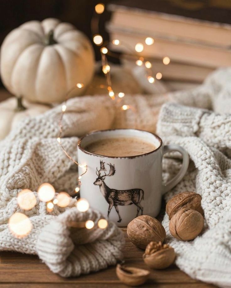 a cup of coffee sitting on top of a wooden table next to nuts and pumpkins