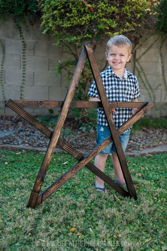 a young boy standing in front of a wooden star sculpture on top of green grass