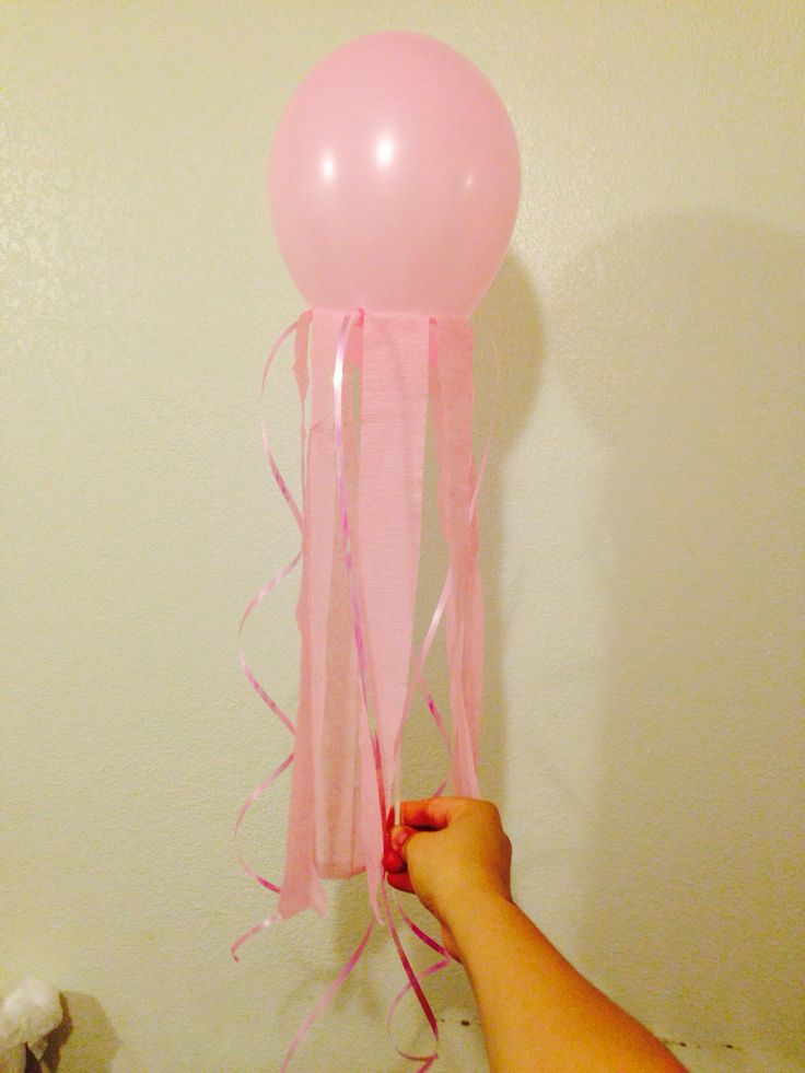 a hand holding a pink balloon with streamers