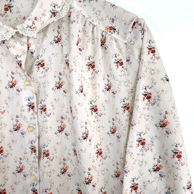 Vintage 1980s floral print blouse with lace trim on the collar and sleeves by Rejoice. Button front. Button sleeves. Yoke with small gathers. Side vents. Lightweight polyester fabric with nice drape. Material / polyester Care / hand wash, hang to dry Suggested modern size / 2X Please check measurements for accurate fit. Make allowance for clothes underneath and room to allow garment to drape properly when worn. Measurements (taken flat on outside, then doubled.) Pit to pit 48" Waist 48" Sleeve, Collared Blouse With Floral Print For Daywear, Daywear Button-up Blouse With Floral Print, Feminine Ditsy Floral Print Blouse For Daywear, Floral Print Tops With Peter Pan Collar For Daywear, Cottagecore Floral Print Blouse For Daywear, Vintage White Floral Print Blouse, Vintage White Blouse With Floral Print, Retro Floral Print Blouse For Daywear, Lace Trim Blouse