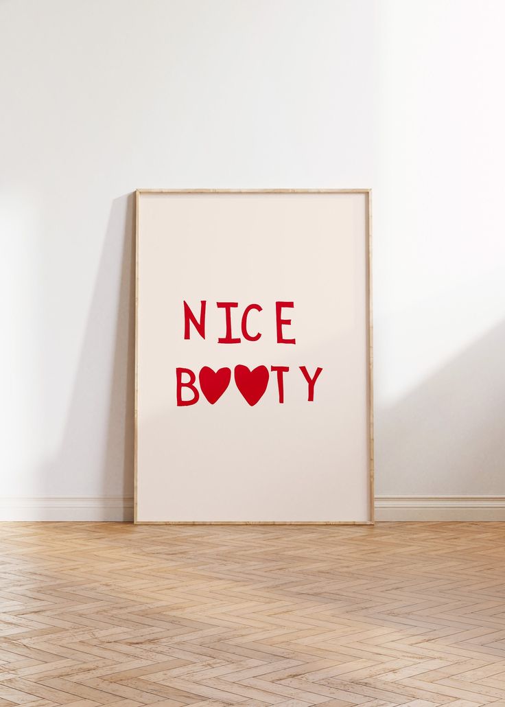 a white framed poster with the words nice body in red on it, against a wall