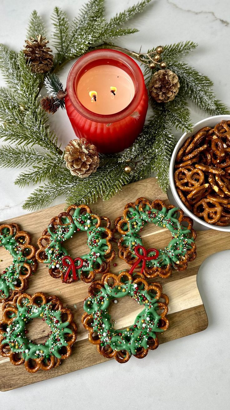 some cookies are sitting on a cutting board next to a candle and bowl of pretzels