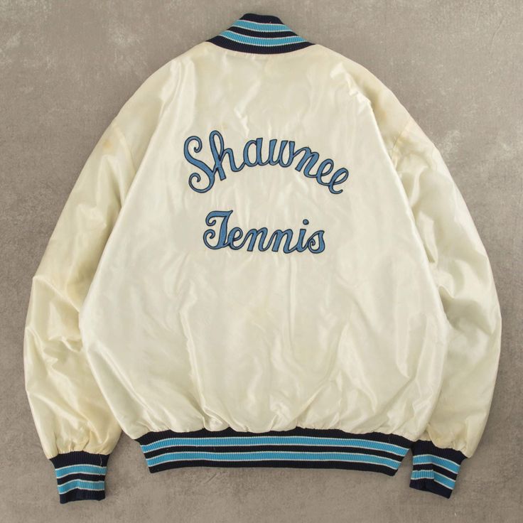 Women's Vintage 1990s Shawnee Tennis Satin Bomber Jacket  + Damage: Minor Marks  + Tag: DeLong  + Made In USA  + Outer Material: Nylon / Lining Material: Polyester  + Colour: Off-White  + Size Label States: Large  + Recommended Size: Large  + Measurements (Inches): Pit To Pit = 24, Body Length = 26  Please note that all vintage items have been previously worn, and may show some signs of previous wear. However, any significant damage will be photographed and/or stated in the items listing. Please note that damage to the inside may not always be photographed or listed. White Vintage Track Jacket For Spring, Vintage White Outerwear For College, Retro Varsity Jacket For Spring Sports, Retro Varsity Jacket For Sports In Spring, Retro Spring Varsity Jacket For Sports, White Vintage Windbreaker For Fall, Vintage Long Sleeve Track Jacket For Spring, Vintage Varsity Jacket For College In Spring, Vintage White Windbreaker For Fall