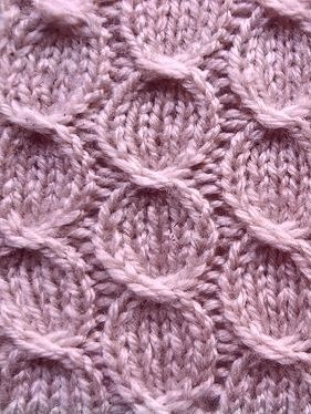 a close up view of a pink knitted blanket with circles on the top and bottom