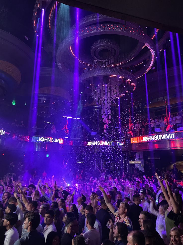 a large group of people at a party with purple lights and confetti on the ceiling