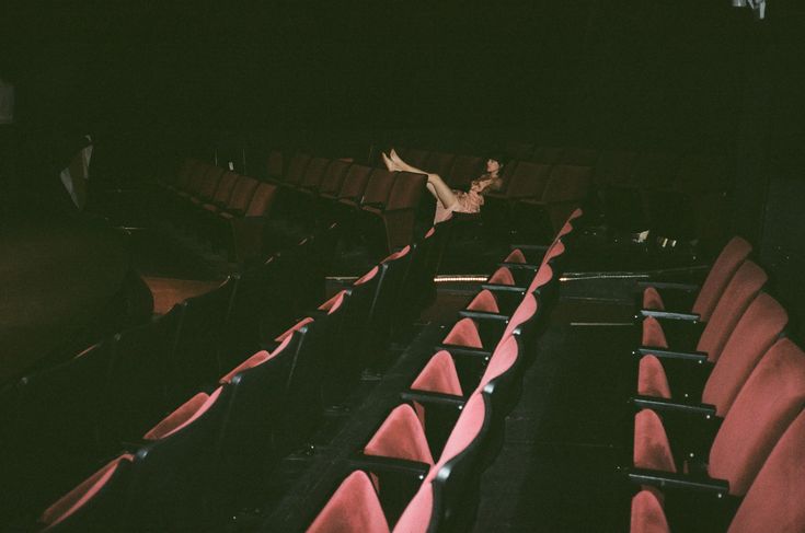 a woman is sitting in an empty theater with her legs spread out on the seats