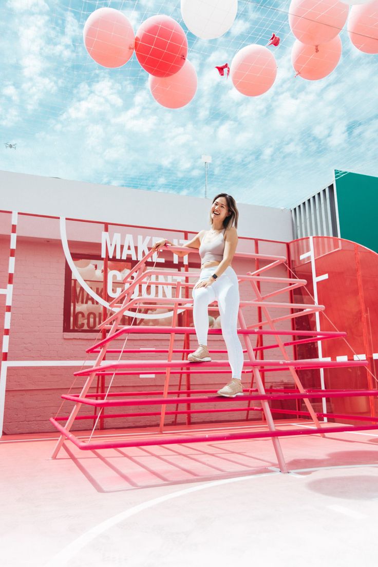 a woman standing on top of a red and white ladder in front of some balloons