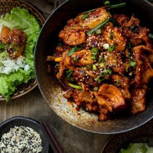 a bowl filled with meat and vegetables on top of a wooden table next to rice