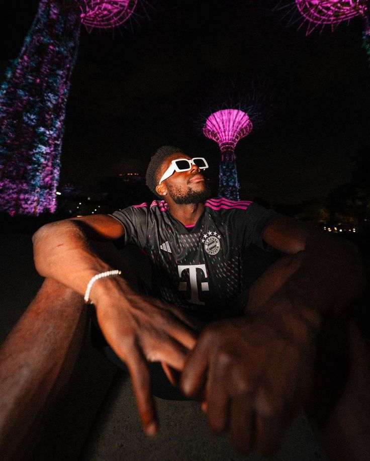 a man wearing sunglasses sitting in front of trees with purple lights on them at night