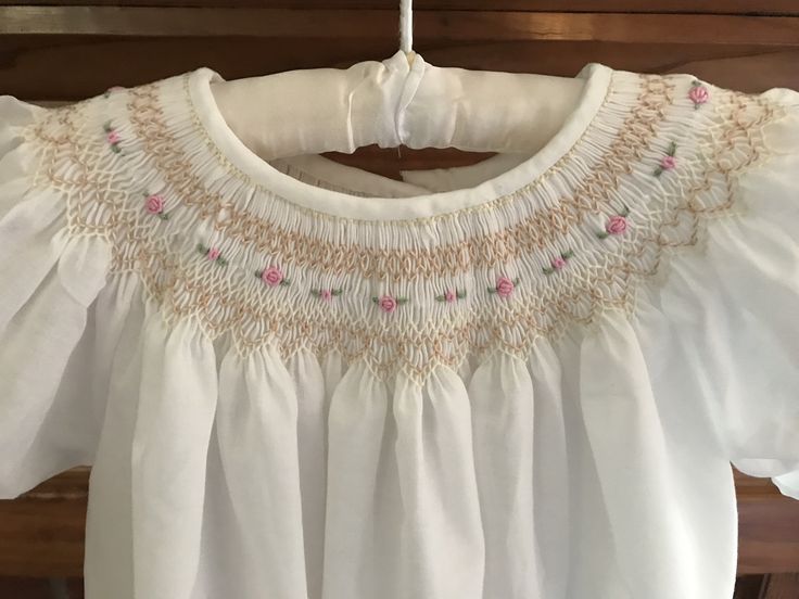 a white blouse with pink flowers on the chest and collar, hanging from a wooden hanger