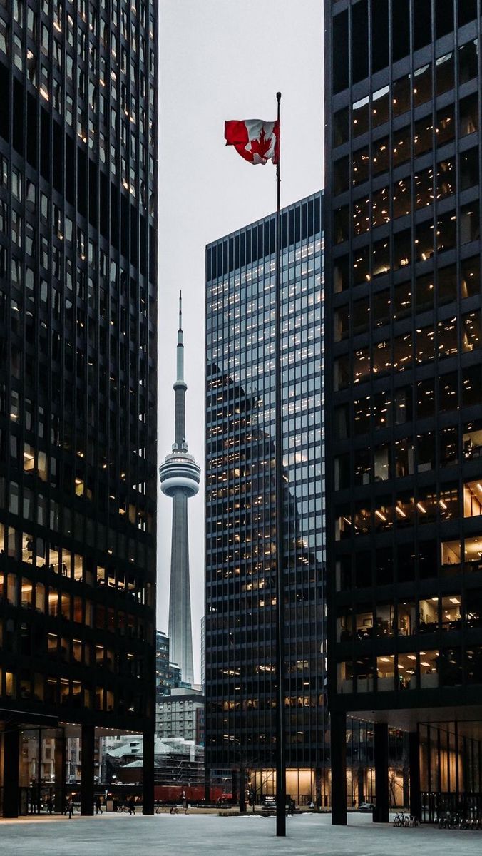 the canadian flag is flying high in the sky above some tall buildings and skyscrapers