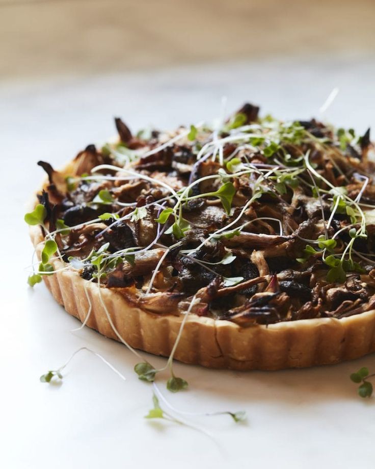 a pizza topped with mushrooms and sprouts on top of a white countertop