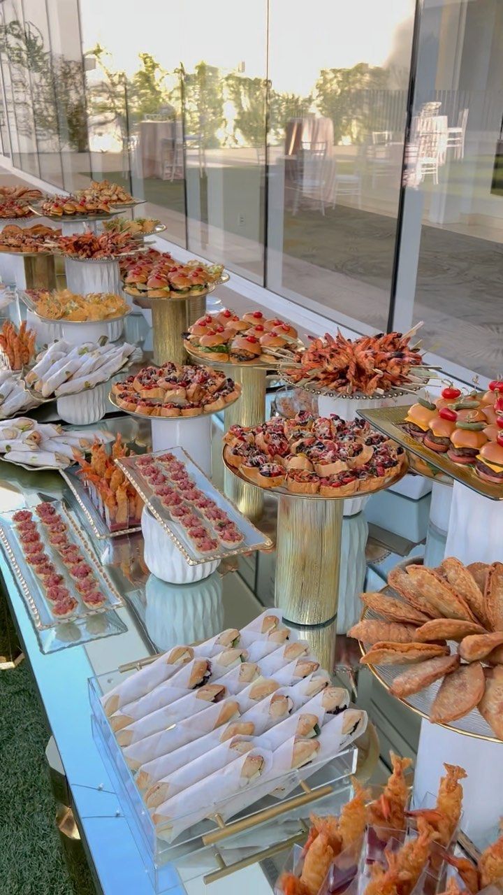 a table filled with lots of food on top of a glass covered buffet area next to a building