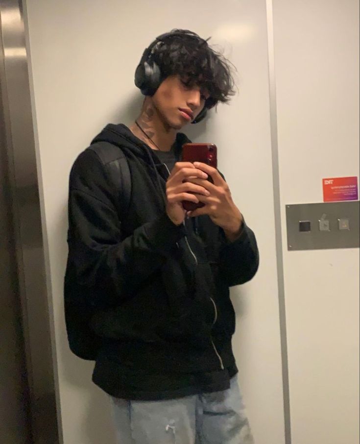 a young man wearing headphones is looking at his cell phone while standing in an elevator