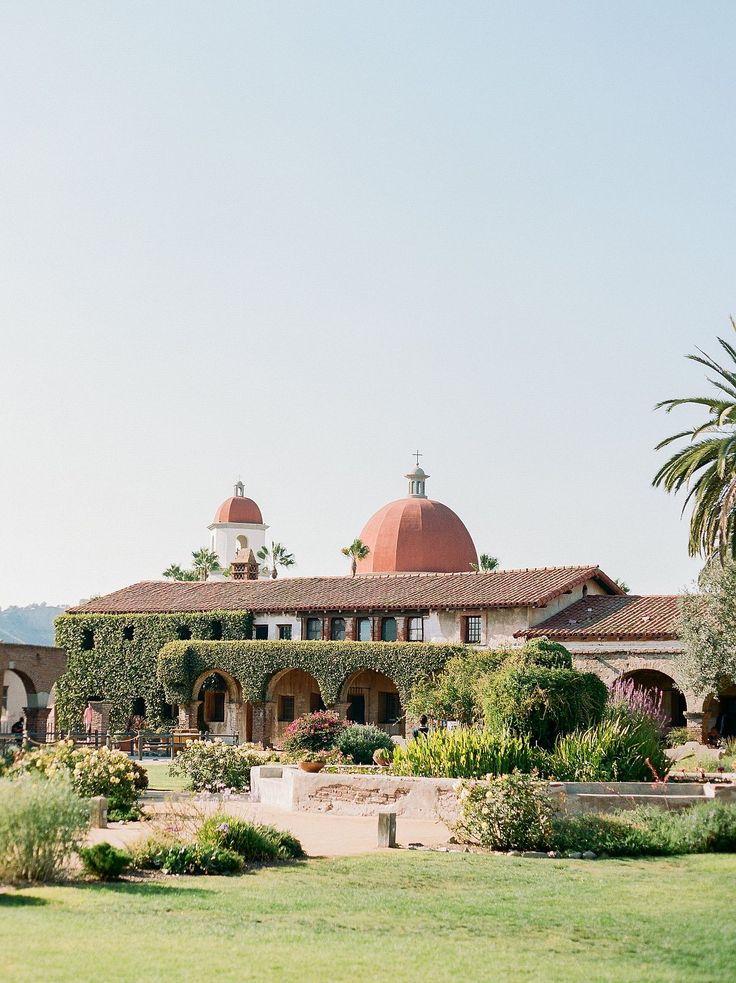 a large house covered in vines and surrounded by greenery with palm trees on the other side