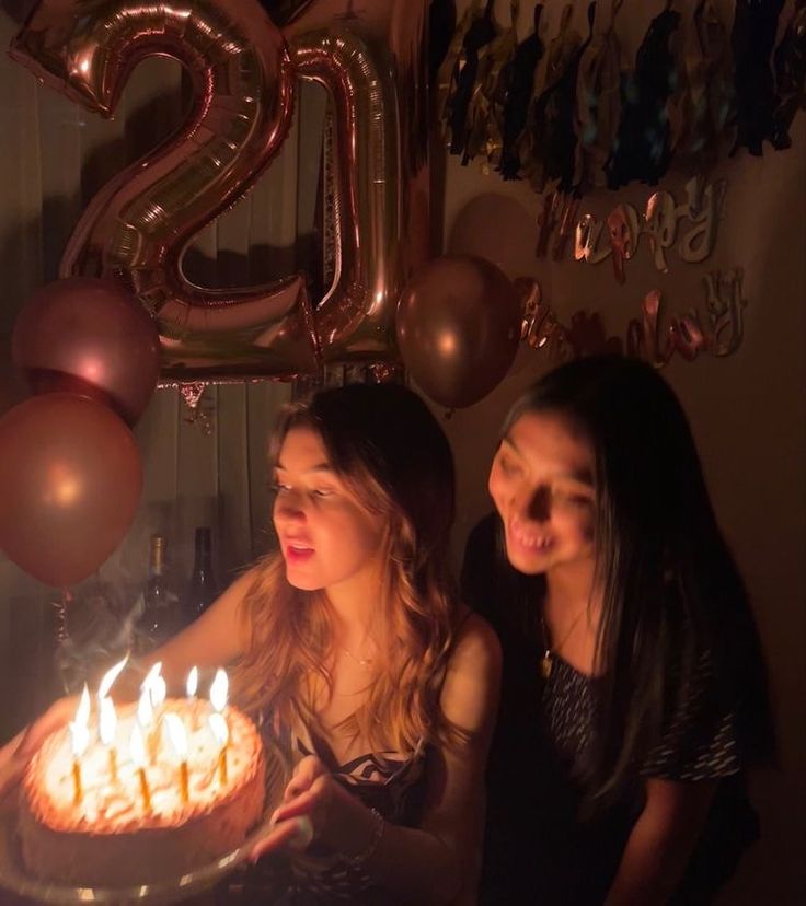 two women standing in front of a cake with lit candles